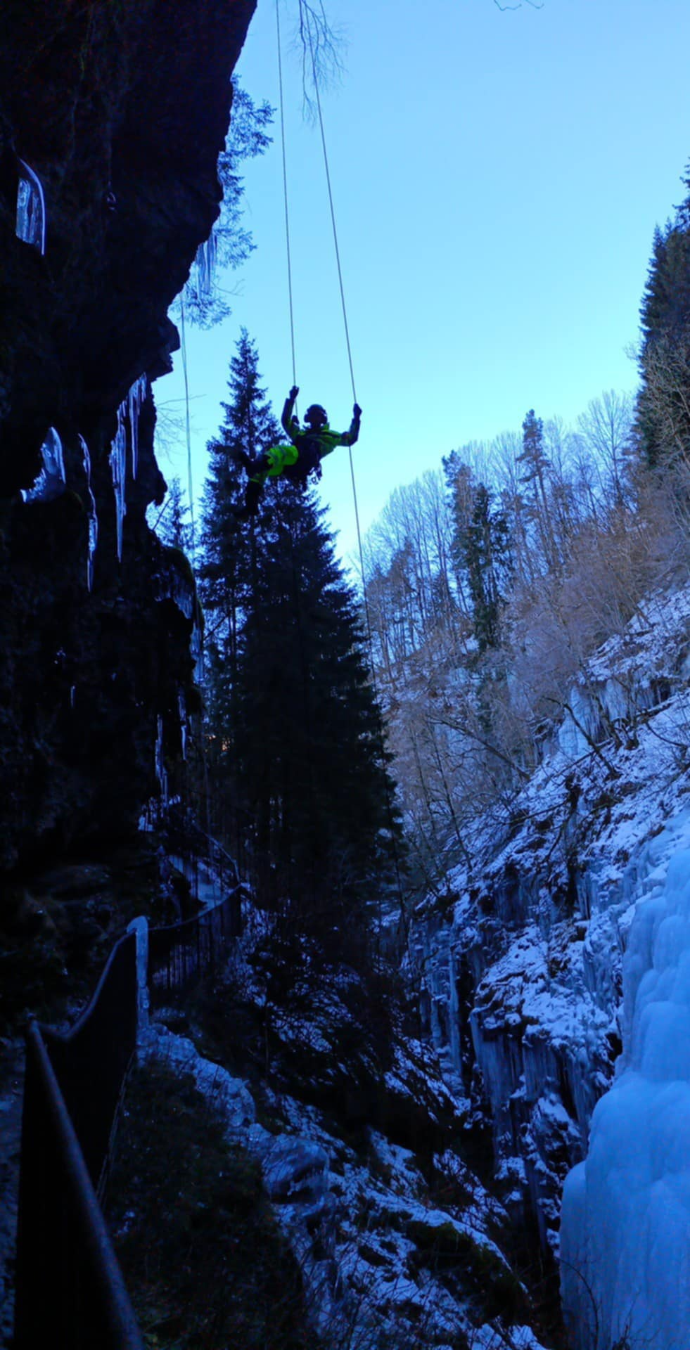 Rope technician suspended on ropes on a frozen rock face during technical rope work.