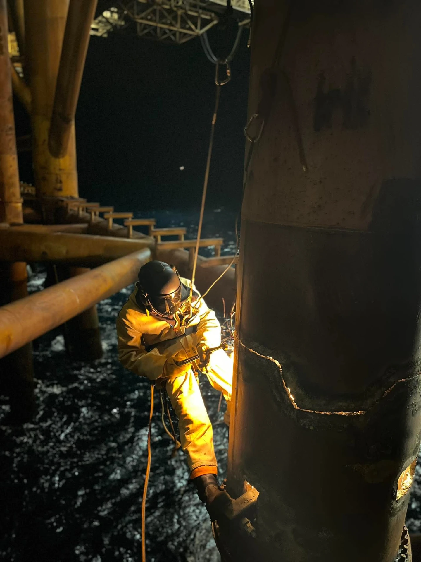 Prosik technician carrying out hot work in ropes beneath an offshore installation at night.