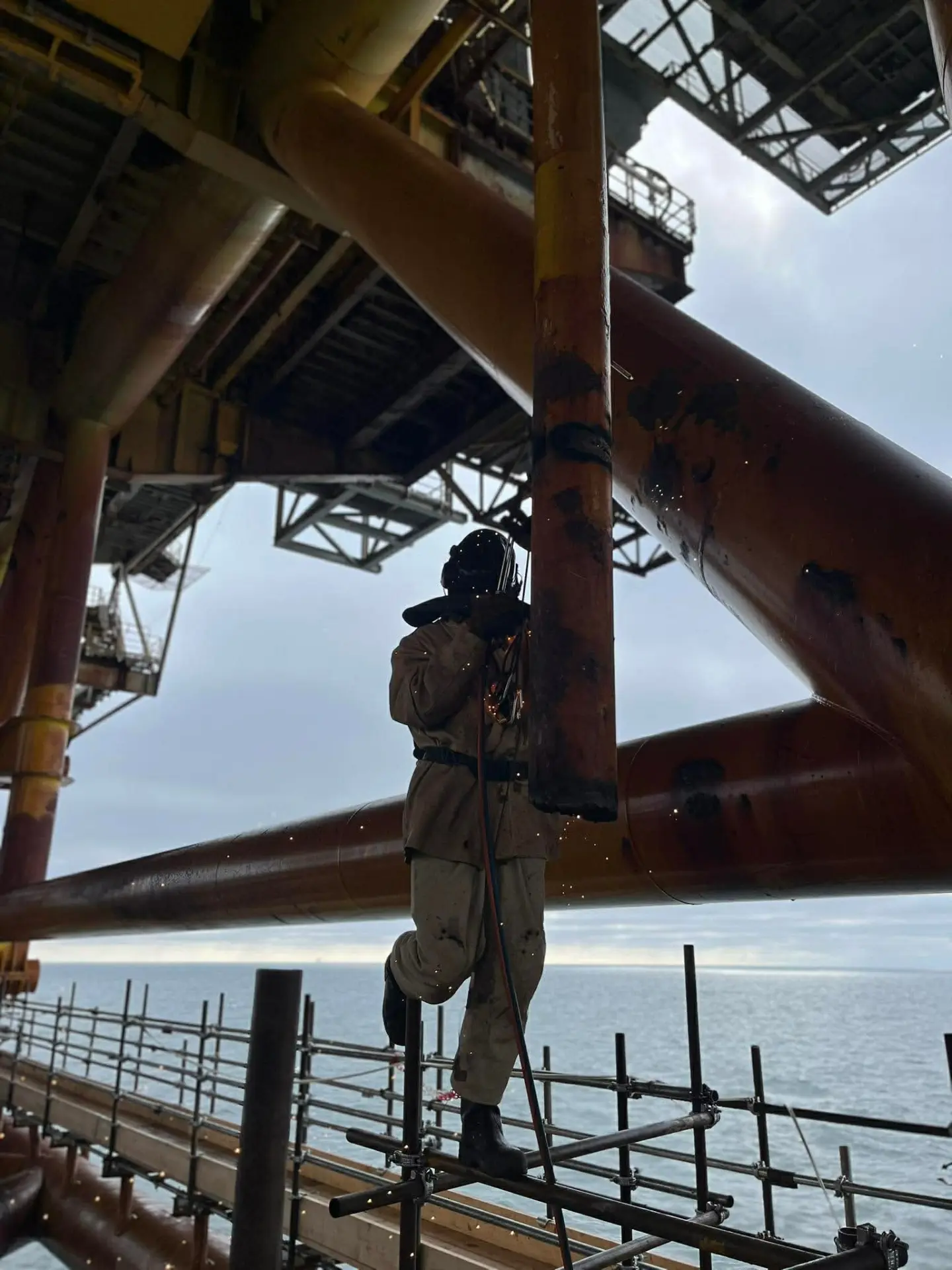 Prosik technician welding on scaffolding beneath an offshore installation in the North Sea.